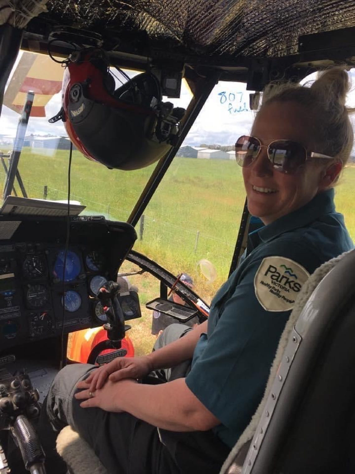 Rhianna sits smiling in the cockpit of a helicopter, wearing her Parks Victoria uniform