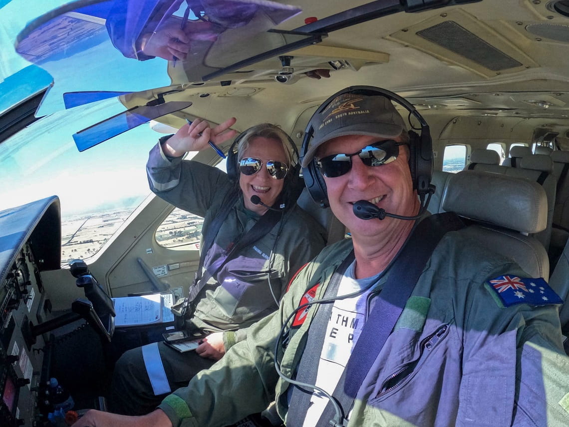 Rhianna and a fellow pilot smiling in the cockpit of a helicopter in the air. 