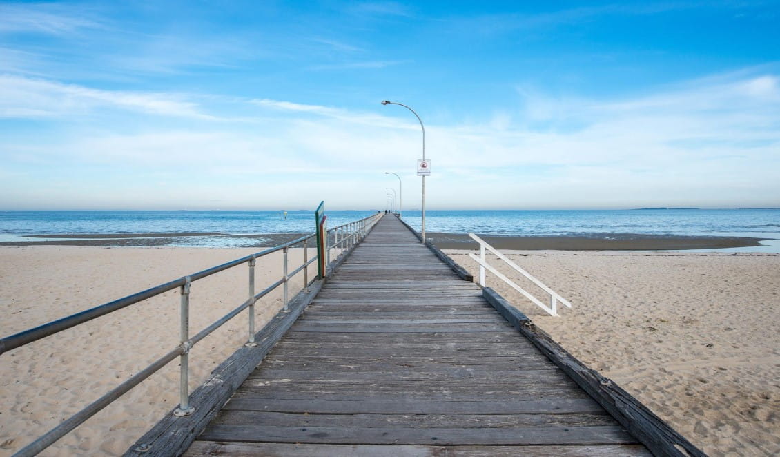 A timber pier stretches out into the water from a sandy beach