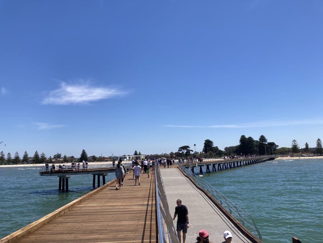 A long pier stretching back towards a beach, with people walking along it.