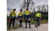 Four people in high-vis carrying tools