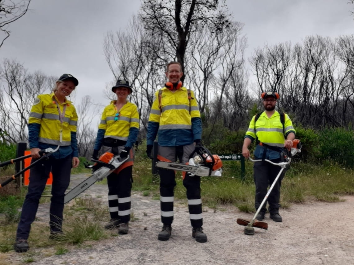 Four people in high-vis carrying tools