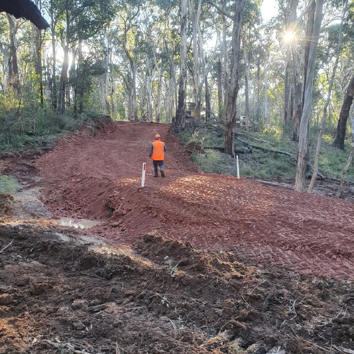 Job well done. A Ranger or worker in a high vis vest is walking away from us on what looks like a new or repaired dirt road. The road is clear of debris and looks new and tidy. 