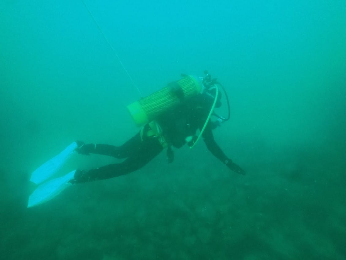 A person in scuba diving gear underwater, reaching out to touch the rocks below them