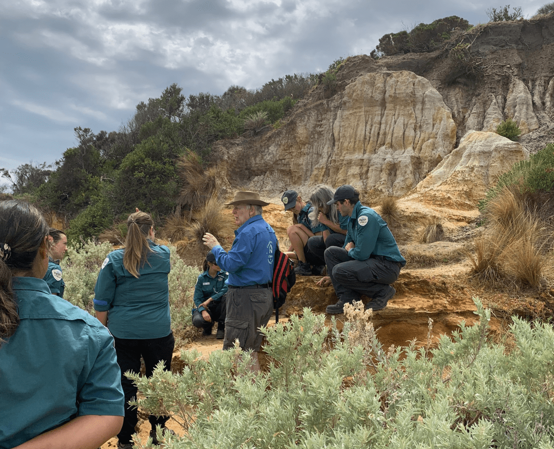 Prof John Buckeridge presenting to rangers in front of cliffs at Ricketts Point Marine Sanctuary