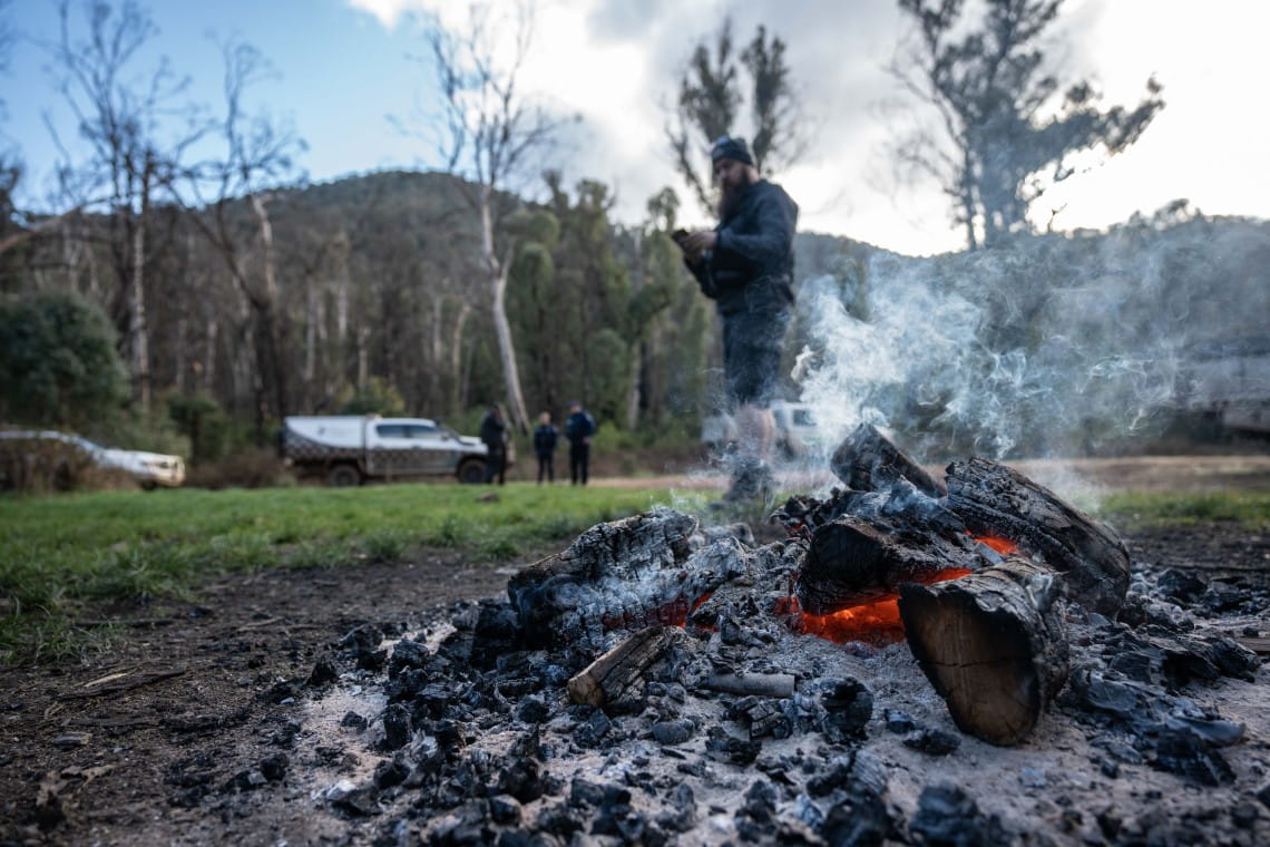A smouldering fire with a Parks Victoria ranger standing nearby.