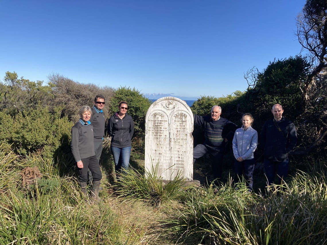 Six people standing next to a large white stone monument shaped like a gravestone.