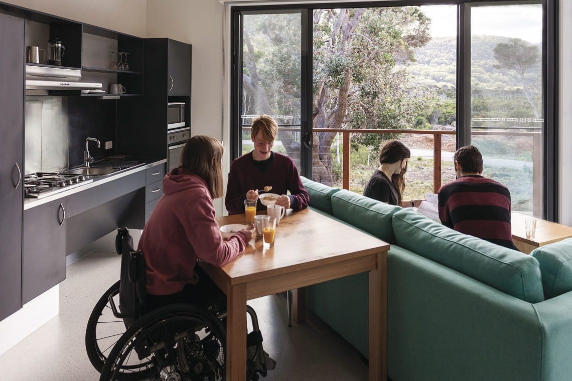Four people sitting in a room together. Female sitting in wheelchair at the table with a male friend.