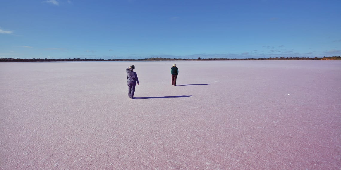 Two people walking away from camera on pink lake in Murray Sunset National Park