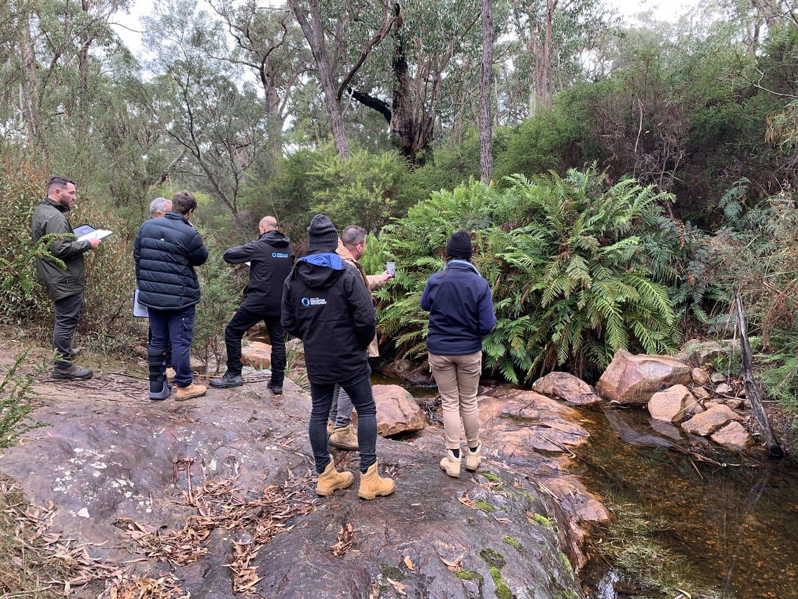 Seven people standing on a large flat rock assessing the crossing damage with folders and phones