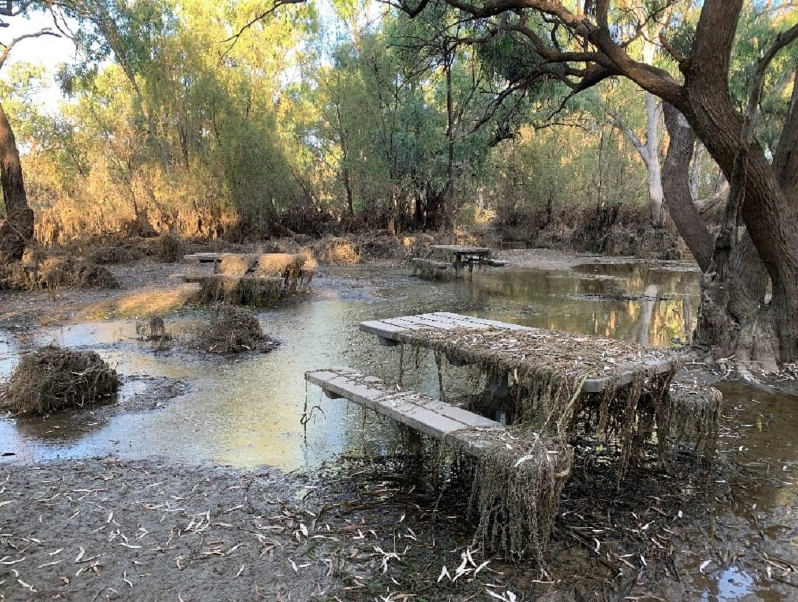 Image shows where floodwaters have started to recede, leaving a picnic area and tables covered in debris