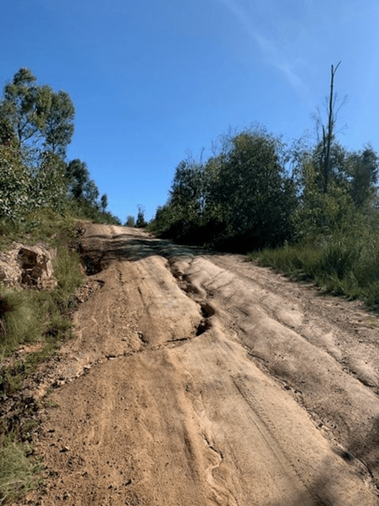 An unpaved road heading up a hill with deep trenches in the surface and standing water 