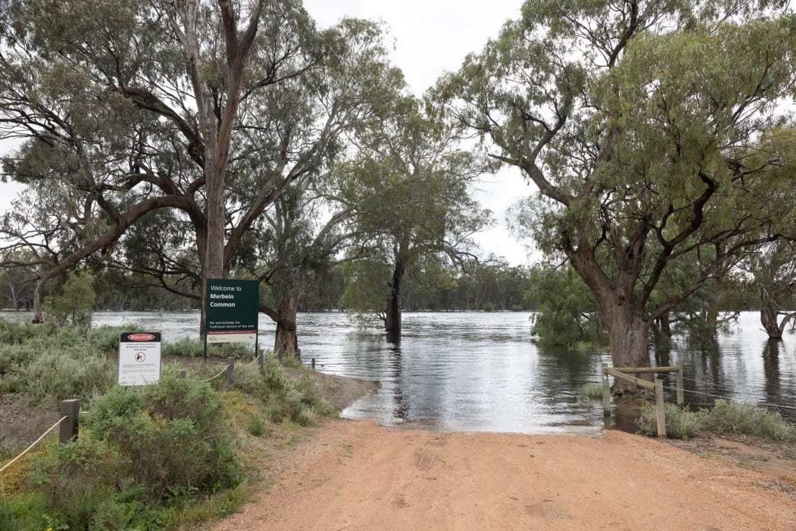 A road leading towards a park sign at Merbein Common is surrounded by riverine flood waters.