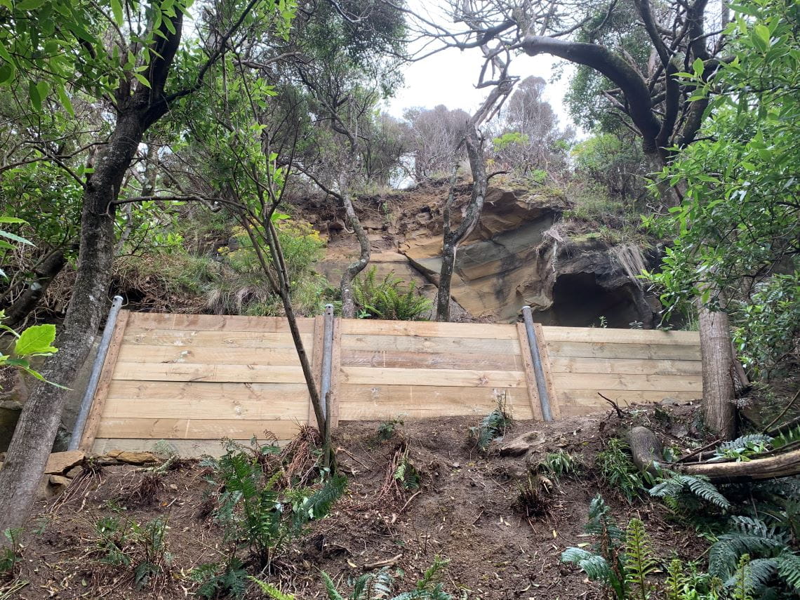 A retaining wall beneath a cliff amid trees.