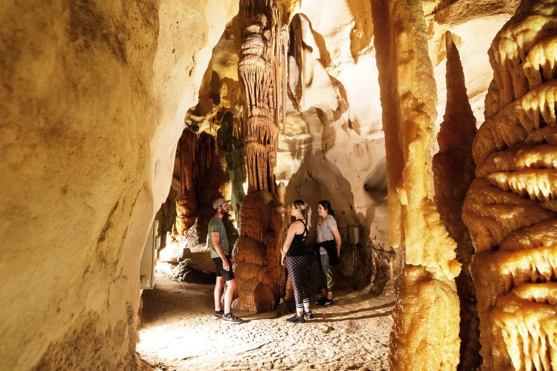 Three friends chat together around a rock formation in an underground cave in Lower Glenelg National Park.