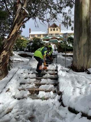 Two park rangers are clearing the snow from the steps leading into the Mount Buffalo Chalet