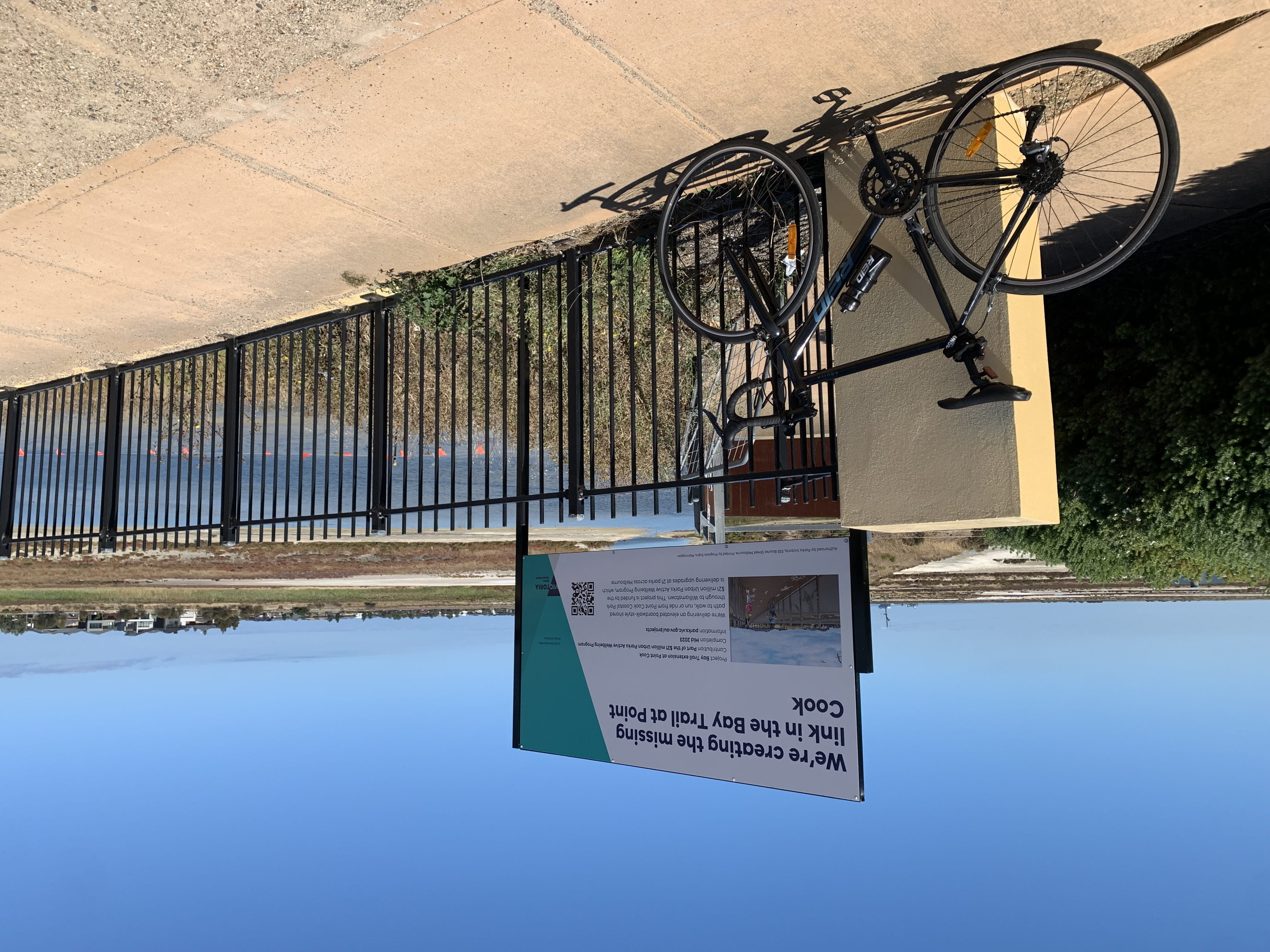 A bike leans against a black metal railing with a sign