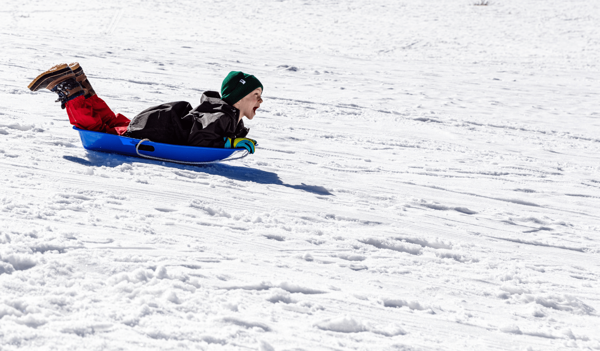 Child riding blue toboggan down snowy slope