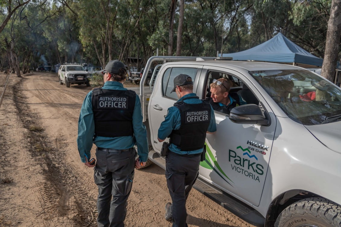 Three men in Parks Victoria uniform stand next to a Parks Victoria truck on a track through forest