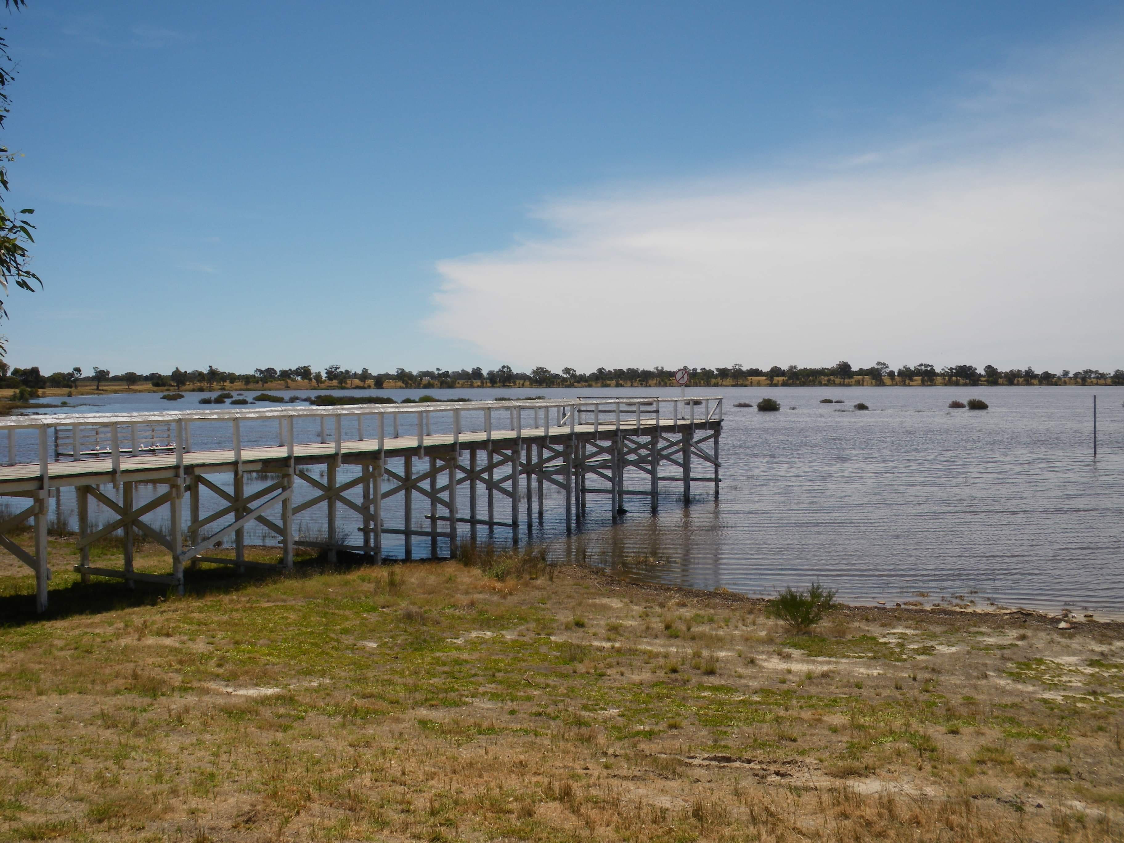 A pier, stretching out into a lake, with an open grassy area in front.