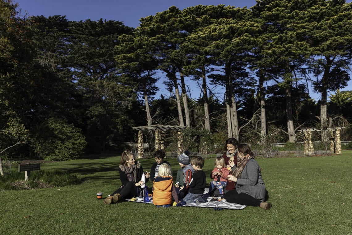 A number of parents and kids sitting down in a picnic blanket using refillable bottles and keep cups
