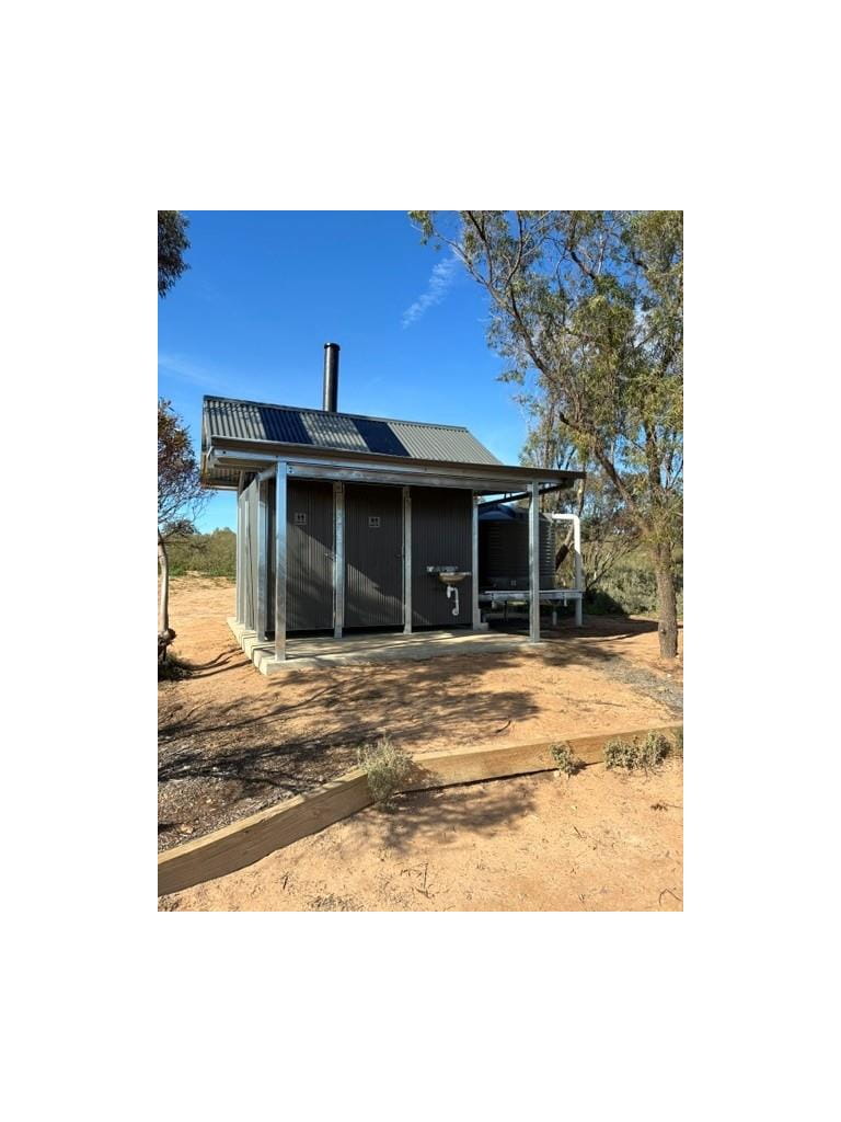 Grey metal two cubicle toilet block with a water tank surrounded by trees