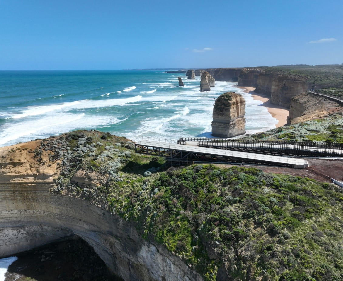 a long walkway under construction with the Twelve Apostles rock formation behind, a wild sea.