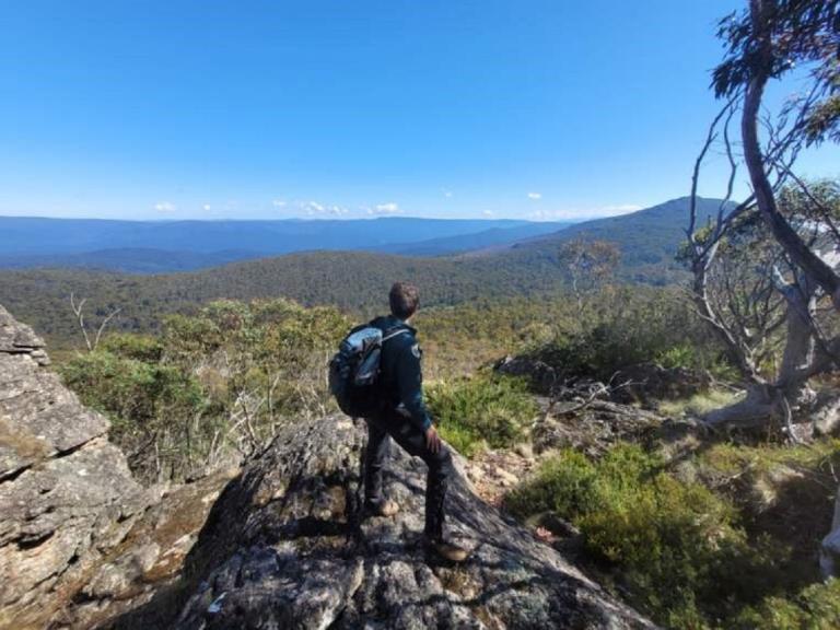 Ranger Jo with her back to the camera, stands on a rock and looks out across the Victorian alps