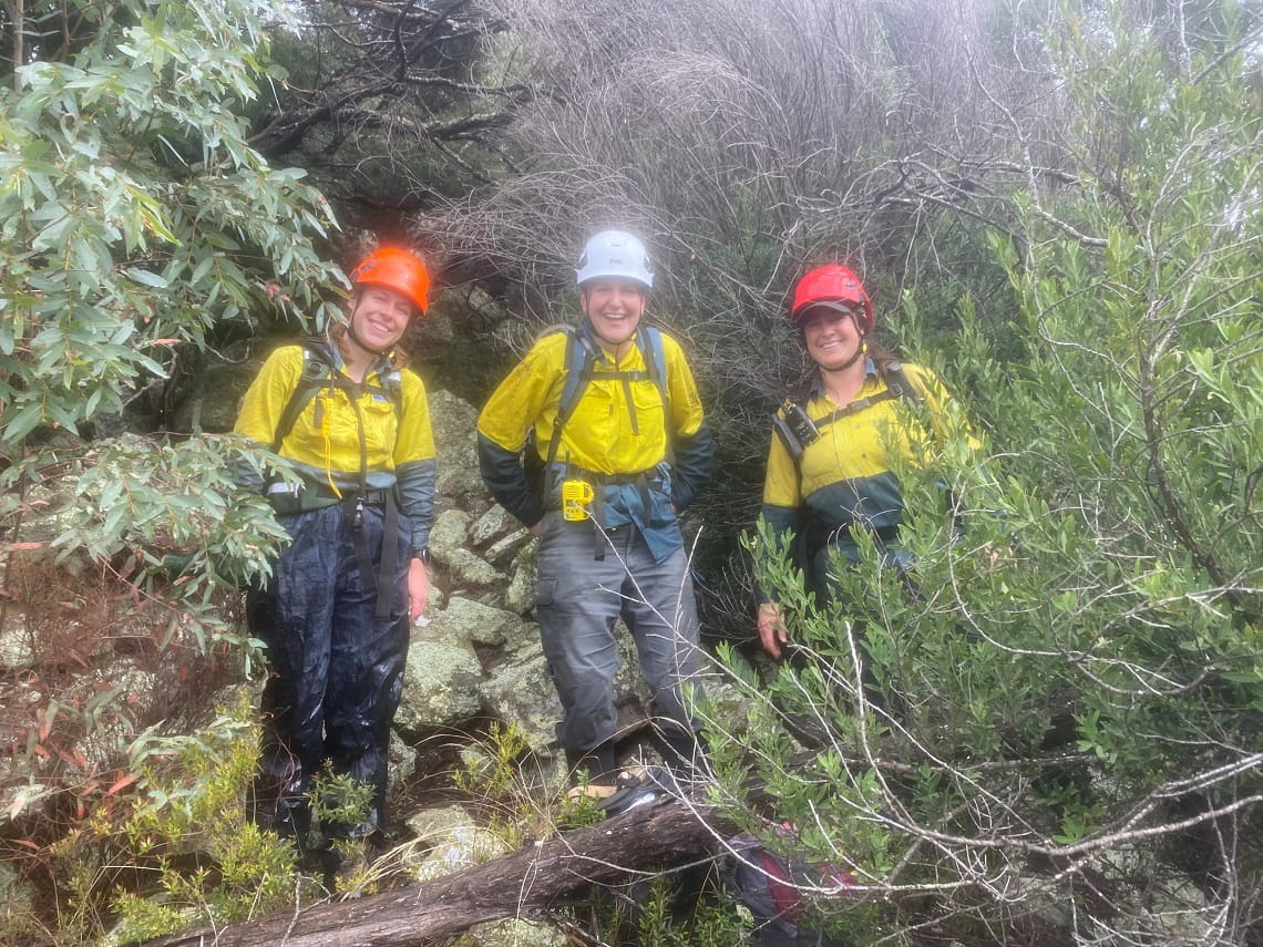 Three rangers stand together among alpine vegetation. They are smiling.