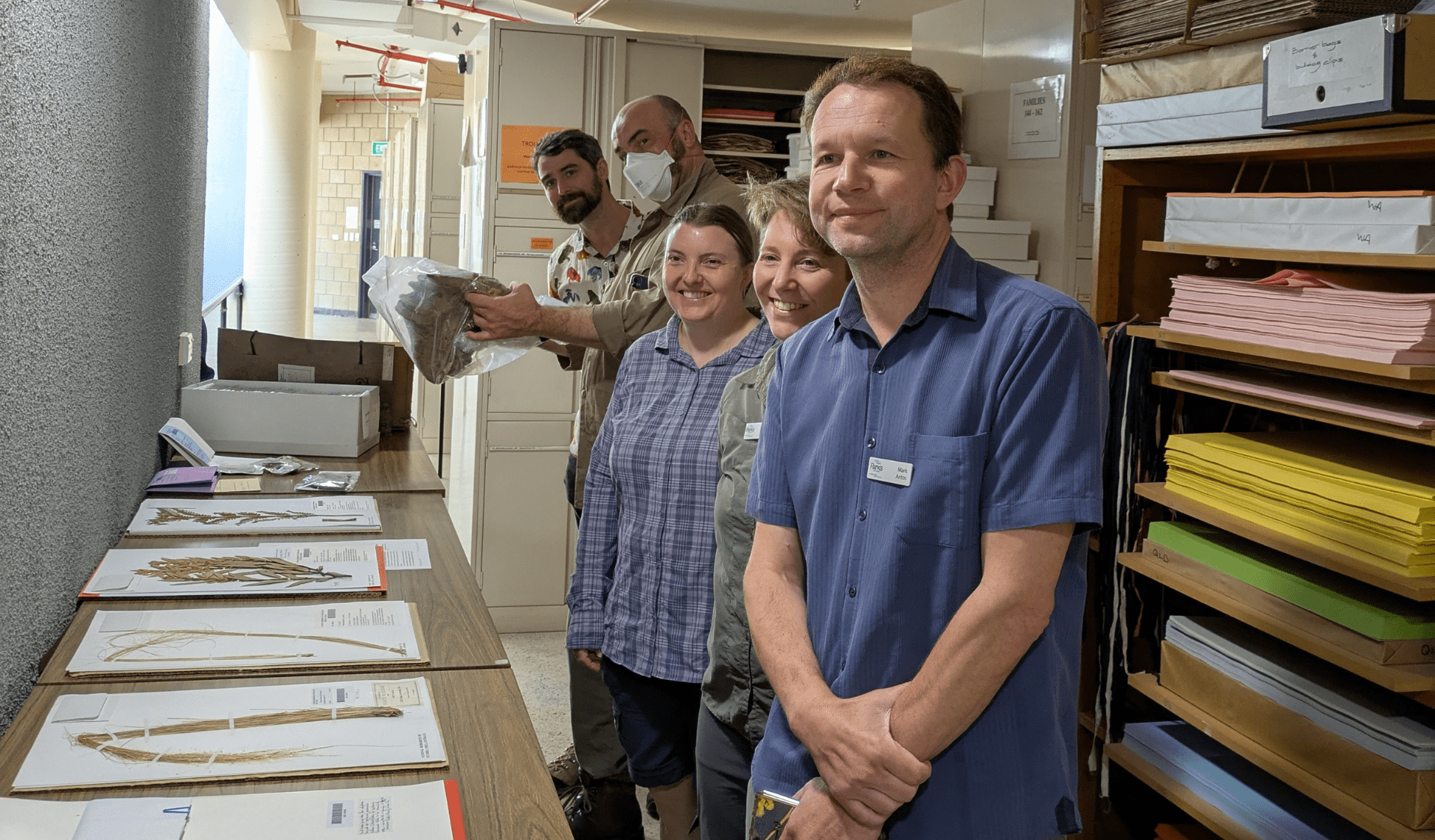 Team of scientists smiling at the camera, in front of them is a lay of specimens 