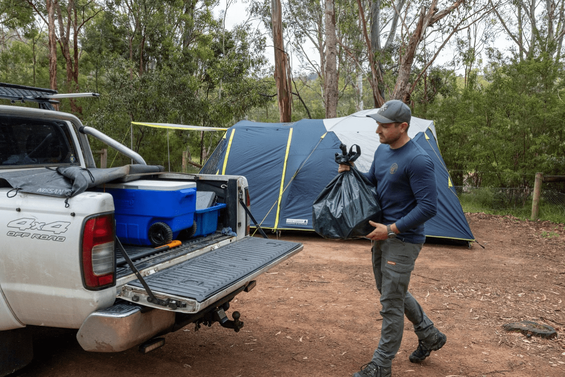 Camper putting a bag of rubbish in the boot of a car