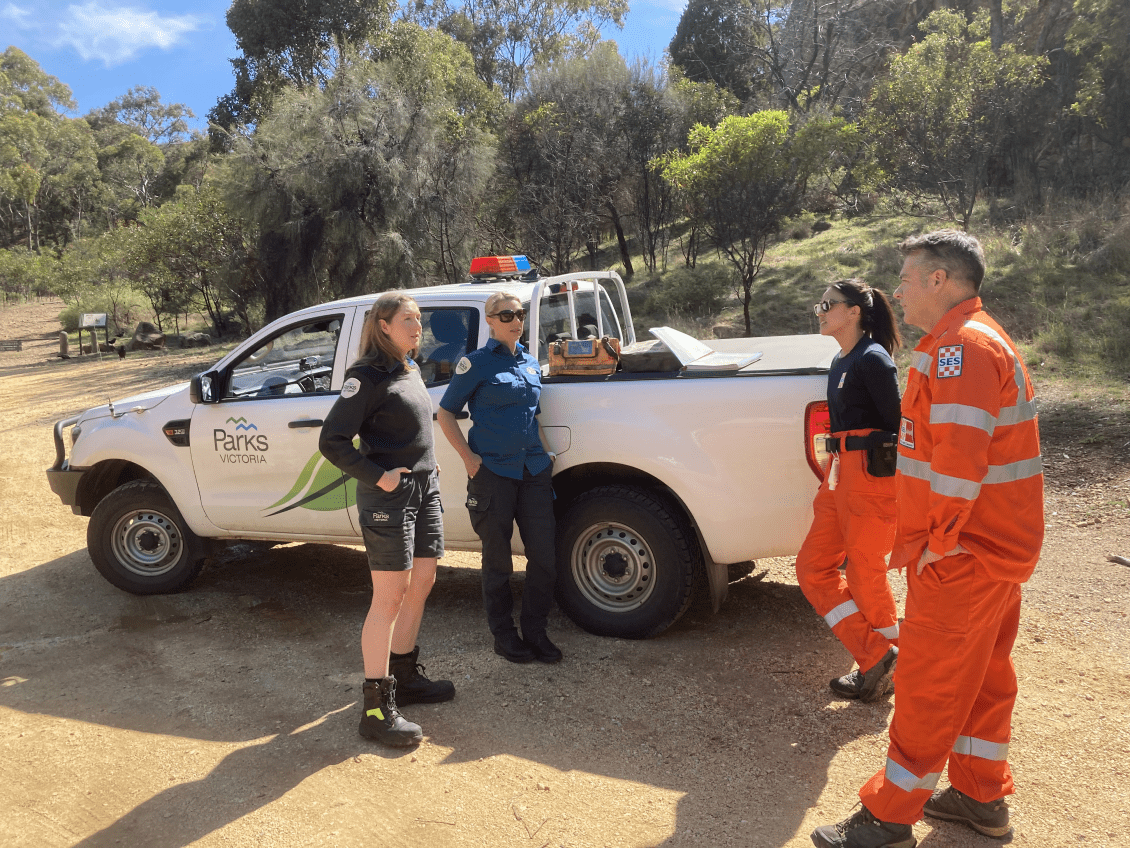 A truck marked "Parks Victoria", two people in Parks Victoria uniform and two in State Emergency Services uniform talking.