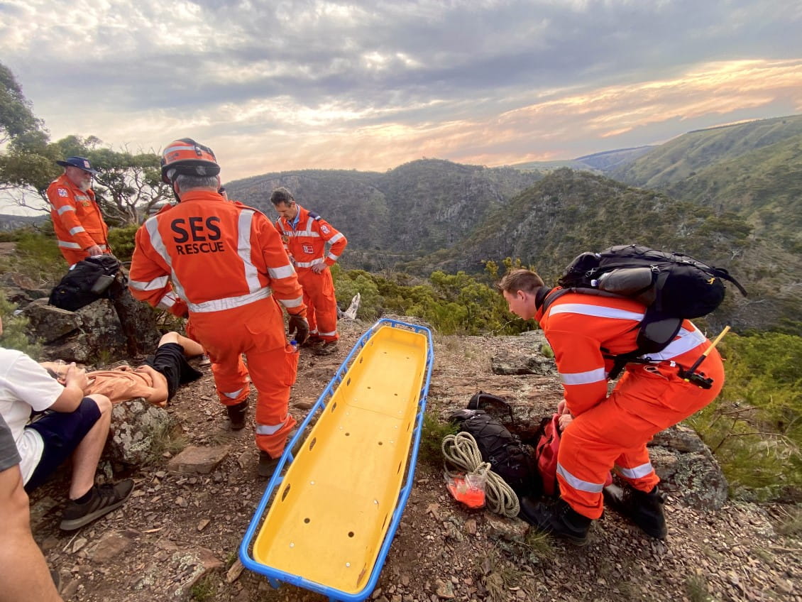 Four men in orange SES uniforms with a yellow stretcher: another man lying to one side hurt.