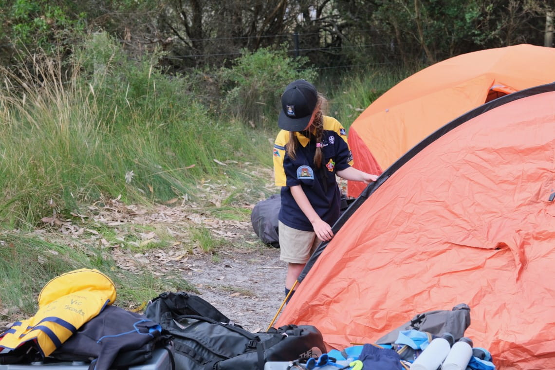 A young girl holding onto tent poles, setting up the tent