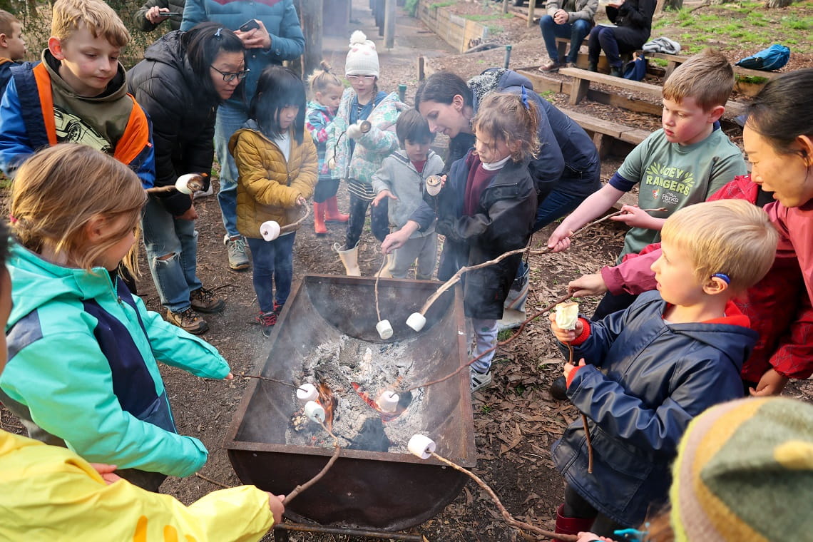 Children gathered around firepit and toasting marshmallows on long sticks
