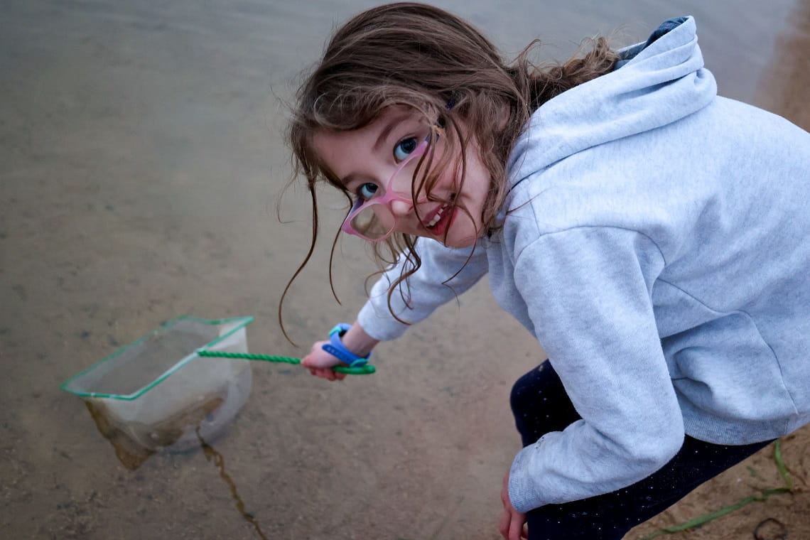 Child playing in the sand catching minibeasts with a net and smiling at the camera