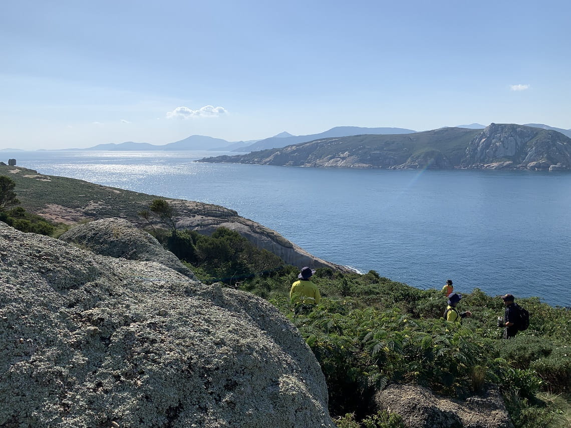 Views of the nearby island are visible, with staff present in the foreground. The blue ocean wraps aroud the islands. 