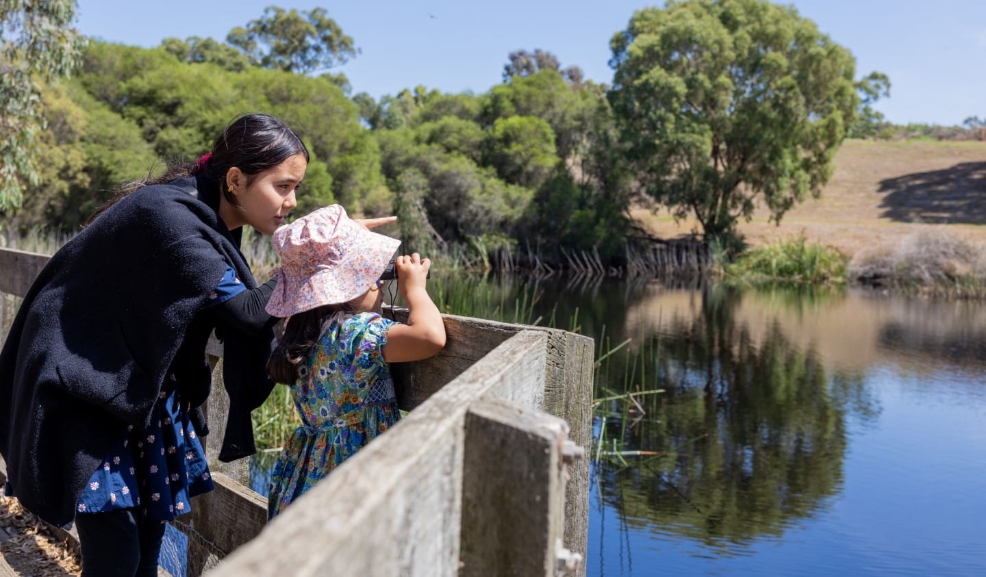 A mother and daughter search for wildlife at a lake.