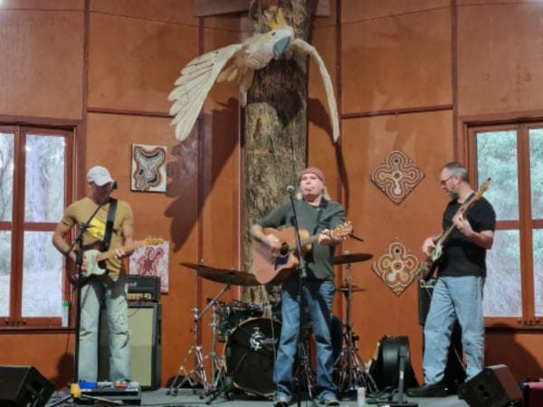 Andy Alberts playing guitar on stage. A guitarist is performing to his right and a bassist on his left.