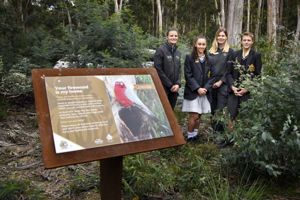 Two students and two Parks Victoria rangers smiling and standing behind signage located at Lederberg State Park