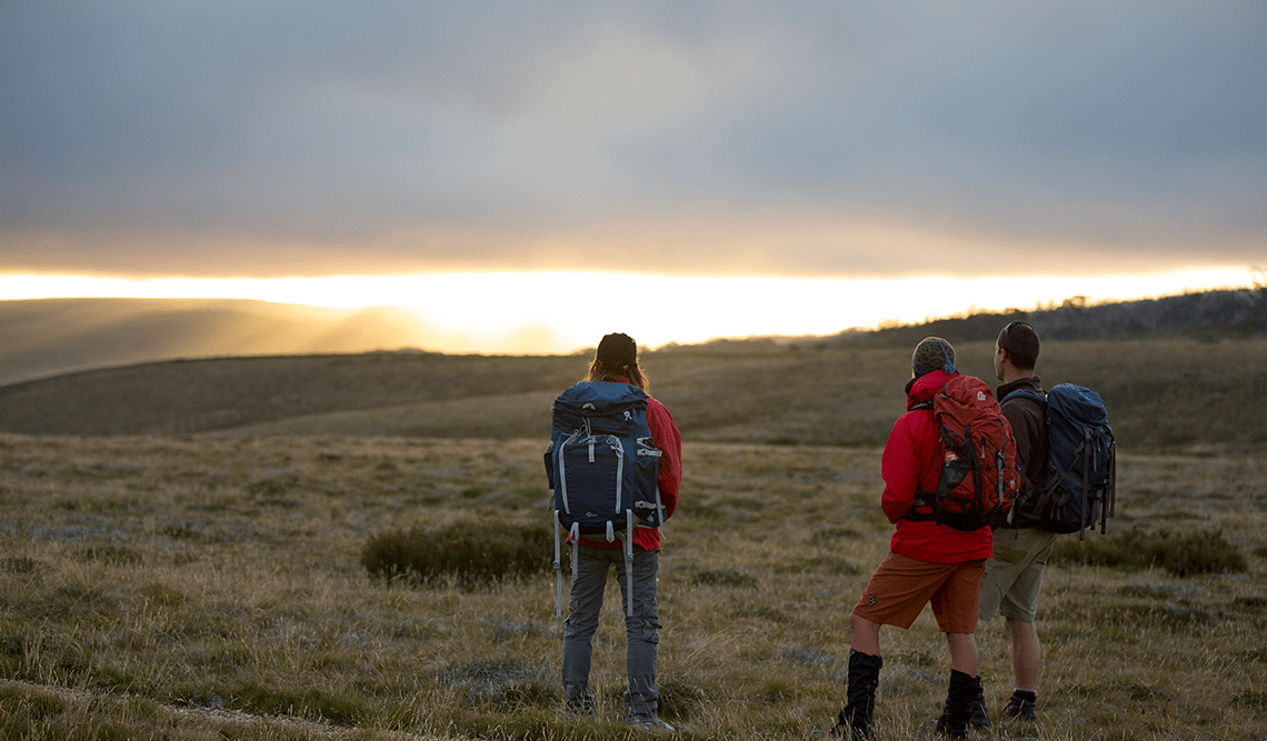 Three people with backs to camera admiring a sunrise on the Falls to Hotham Alpine Crossing