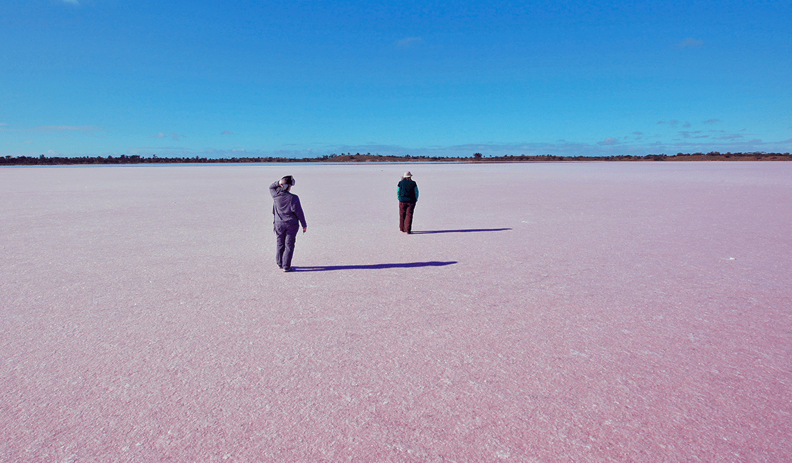 Two women walk on a pink lake at Murray-Sunset National Park