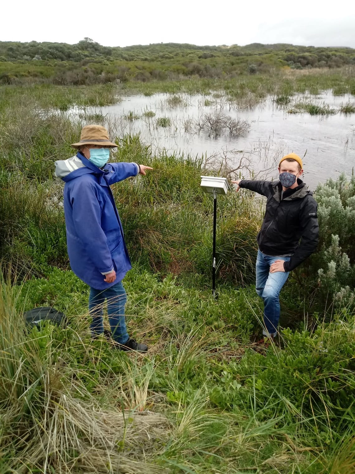 Two volunteers pointing at a new listening post by a swamp