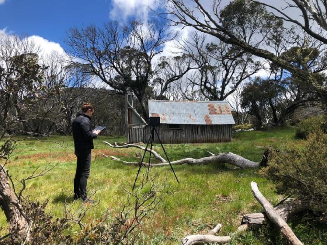 Person standing near a Victorian Alps hut and recording data 