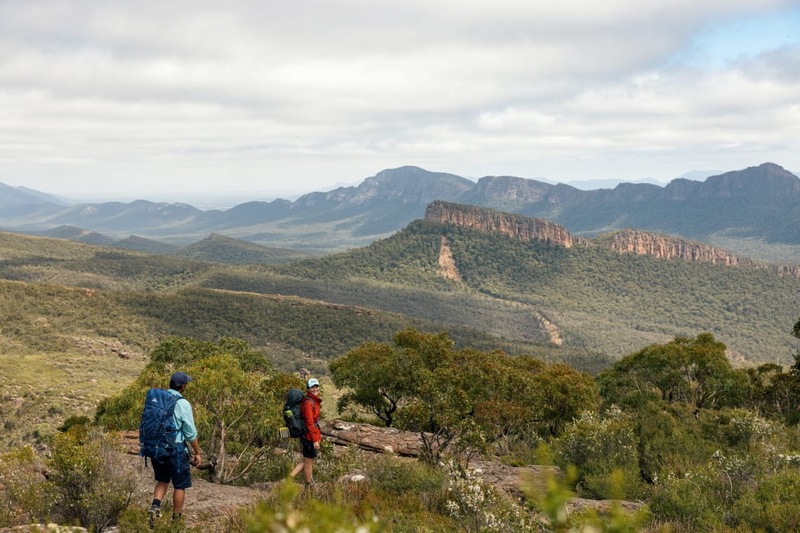 Two hikers walking down an incline. Large rock formations can be seen in the background