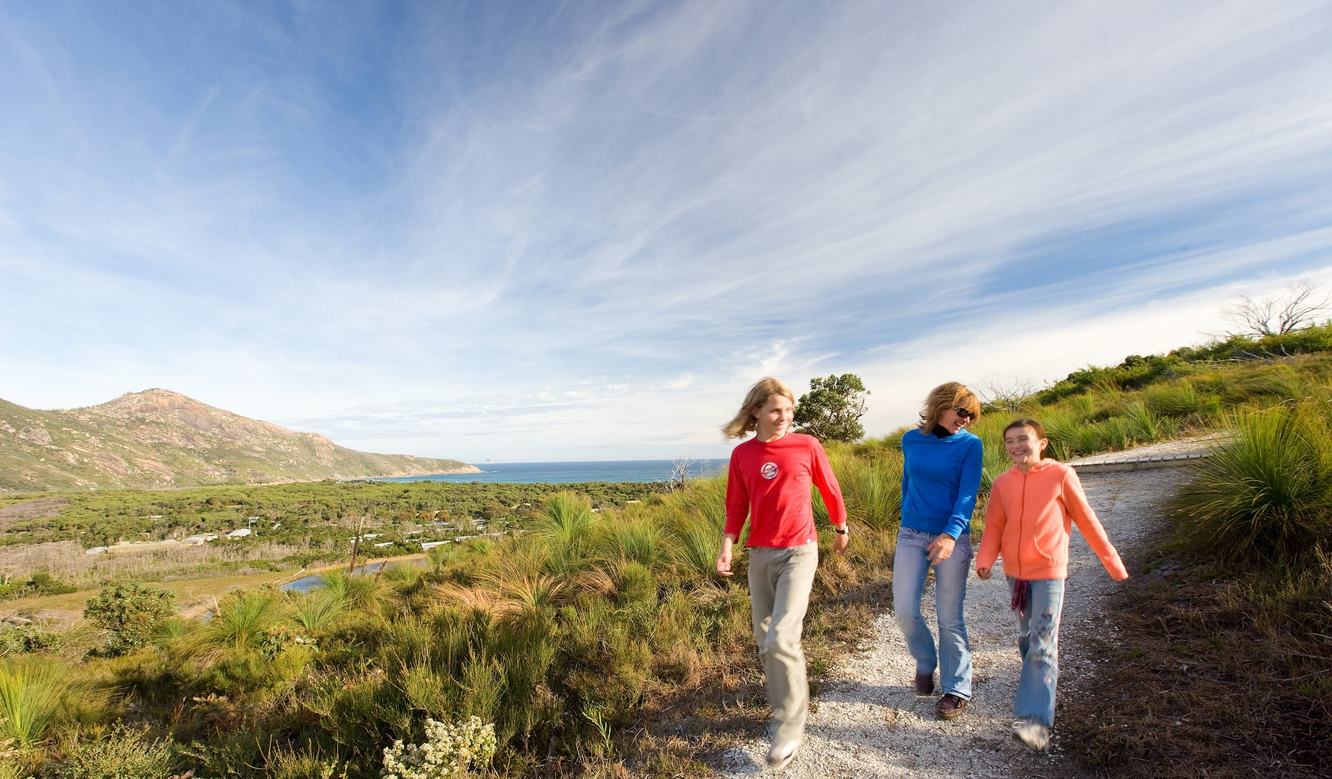 Two children and adult walking along gravel path with ocean views in the background.