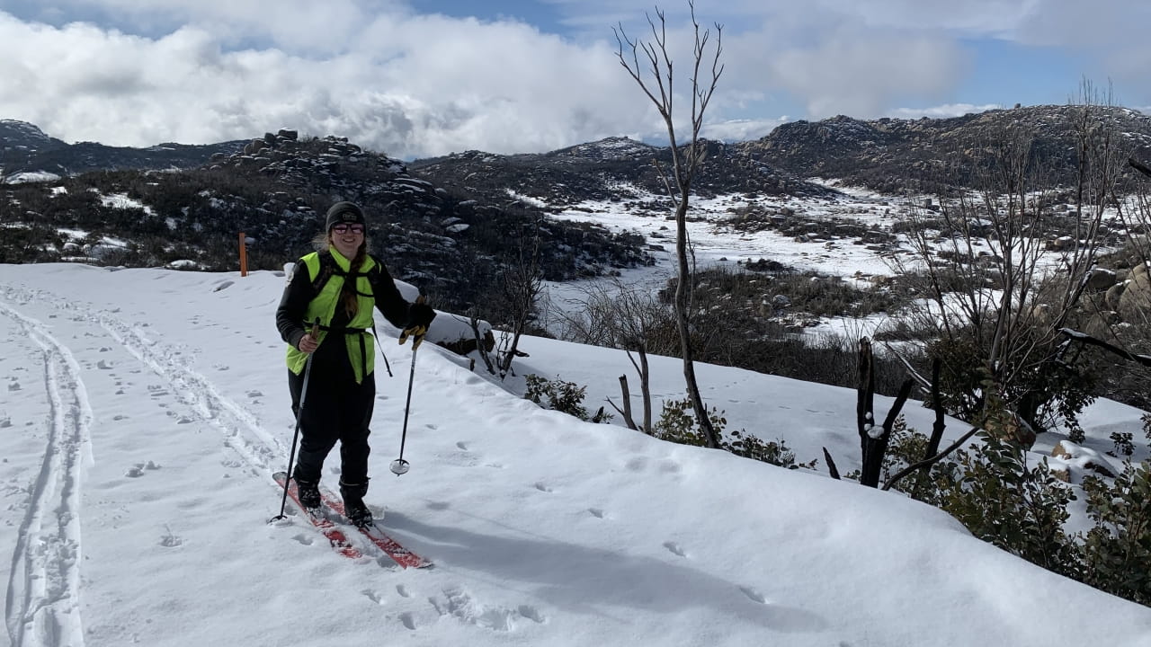A Parks Victoria employee on the slopes of Mt Buffalo, with skis on their feet and poles in their hand