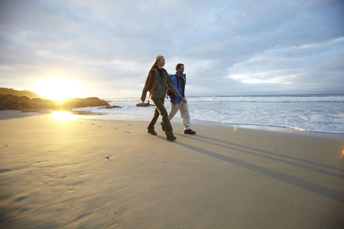 A man and woman walking along a beach in the Yallock-Bulluk Marine and Coastal Park