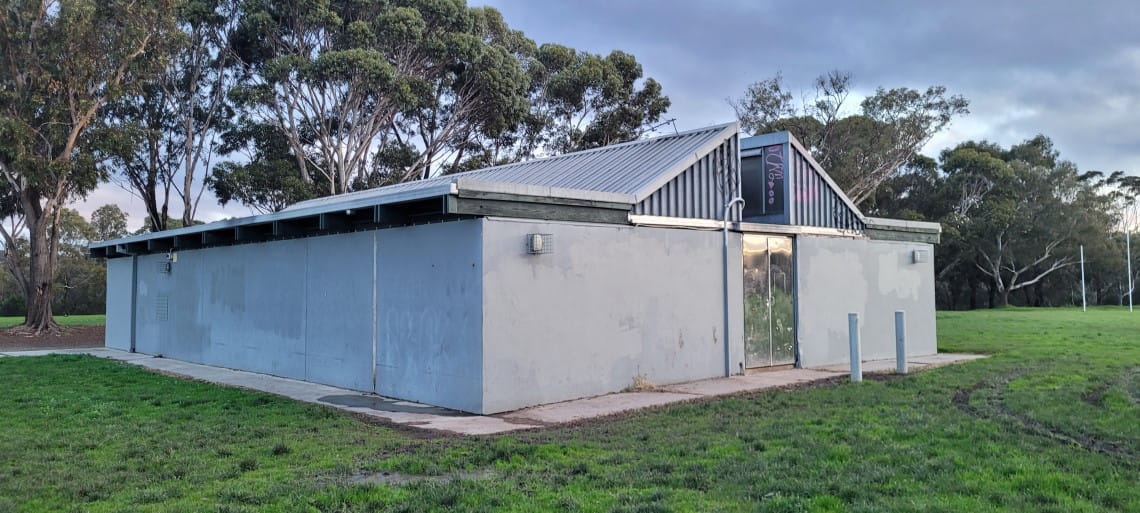 A grey, concrete sports pavilion surrounded by trees and open space