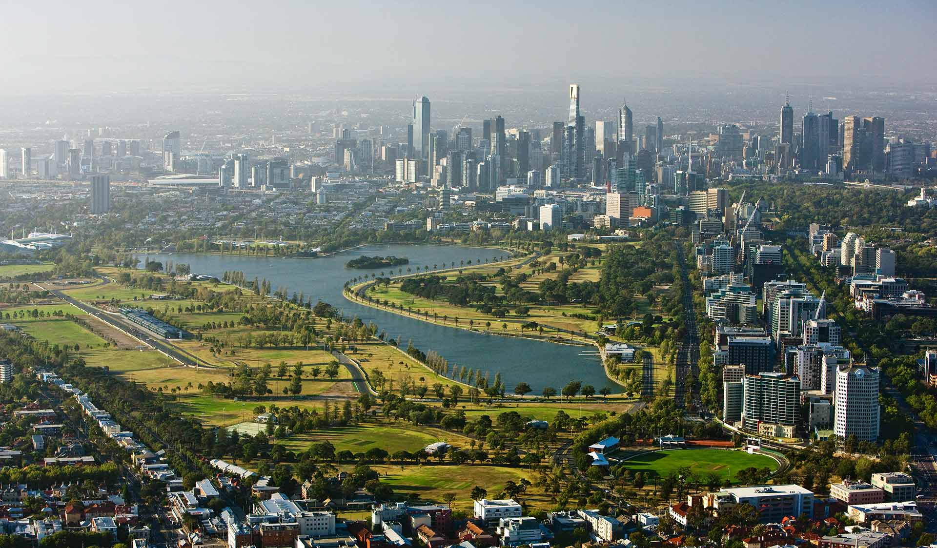 An aerial view of Albert Park Lake with the Melbourne CBD skyline in the background. 